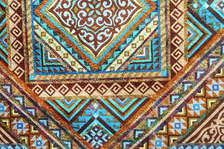 Closeup on a quilt with geometric patterns in blue, brown, tan, and aqua. 
