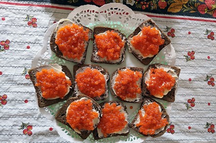 From above, a platter of open-faced sandwiches on dark bread, thick white butter, and small heaps of bright orange, spherical fish eggs.
